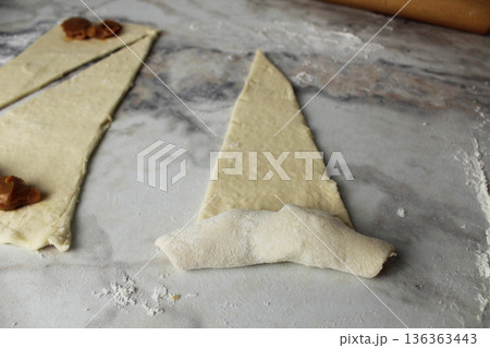A triangle of raw dough is twisted in close-up on a croissant. Homemade cakes 136363443
