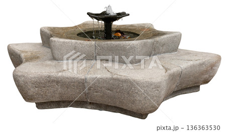 Water flows out from the center of a round stone fountain. The fountain has a unique design with a wide base and is placed outdoors. It is bright with sunlight shining down 136363530