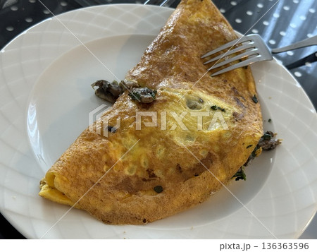 Omelette served on a white plate with a fork, featuring herbs and mushrooms 136363596