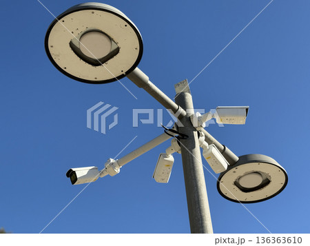 Surveillance cameras and streetlights against clear blue sky background 136363610