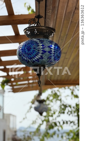 Turkish mosaic lantern with vibrant blue pattern hanging outdoors under wooden pergola background 136363612