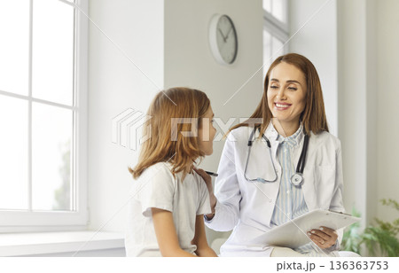 Friendly woman pediatrician with a clipboard talking to a child in the examination room 136363753