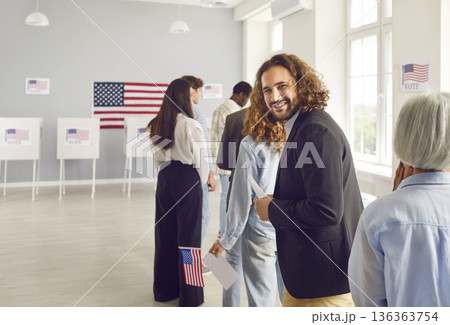 Young happy american voter standing in a queue at vote center and looking cheerful at the camera. Young happy american voter standing in a queue at vote center and looking cheerful at the camera. 136363754
