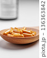 Golden herbal capsules placed in a wooden spoon. Dietary supplement on white table with pills bottle on background 136363842
