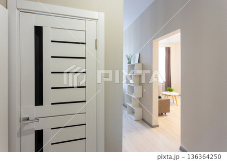 Modern apartment hallway with white interior door and view into a bright living room. Modern apartment hallway with white interior door and view into a bright living room. 136364250