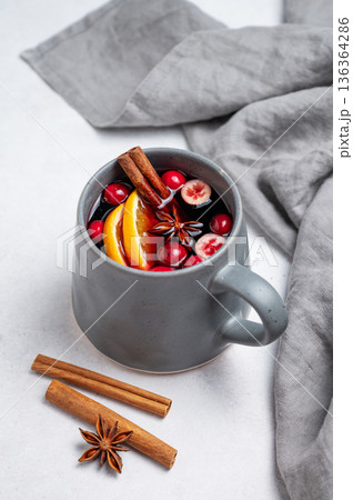 A cup of red mulled wine with cinnamon, orange and cranberry on a light background A cup of red mulled wine with cinnamon, orange and cranberry on a light background 136364286