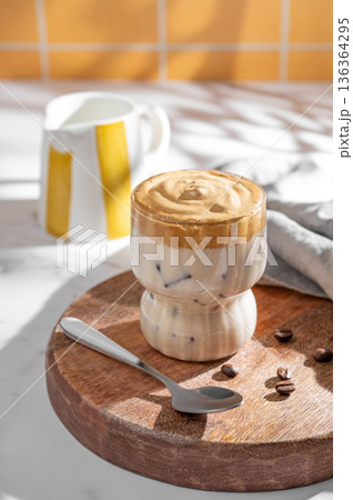 Dalgona coffee on a kitchen orange tile background with coffee beans, milk jug and morning shadows. Dalgona coffee on a kitchen orange tile background with coffee beans, milk jug and morning shadows. 136364295
