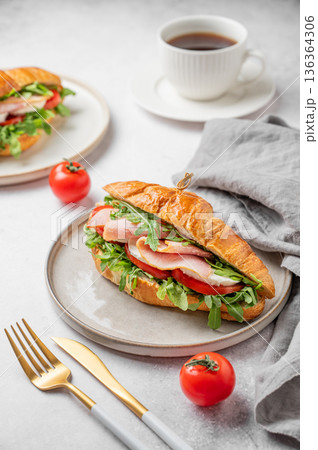 Croissant sandwich with ham, mozzarella cheese, tomato, arugula on a plate and cup of coffee Croissant sandwich with ham, mozzarella cheese, tomato, arugula on a plate and cup of coffee 136364306