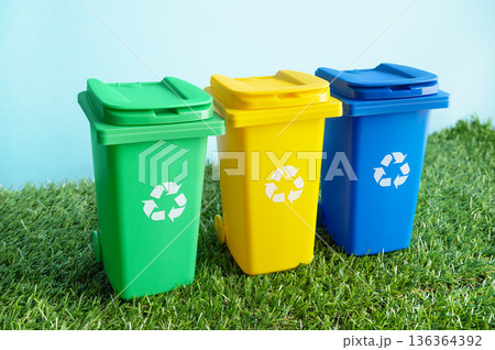 Colorful recycling bin on grass over blue background. Three waste separation containers promoting eco friendly living and environmental awareness. Waste management, clean environment concept. 136364392