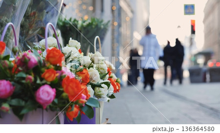 Colorful flowers on city street with blurred people walking by in background 136364580