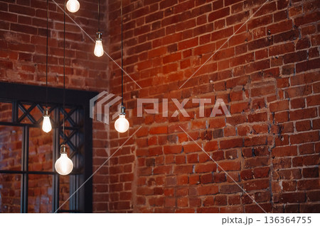 Hanging light bulbs on cables against red brick wall interior with copy space Hanging light bulbs on cables against red brick wall interior with copy space 136364755