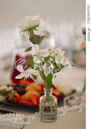 White flowers in small glass vase on table in classic room with blurred background White flowers in small glass vase on table in classic room with blurred background 136364761