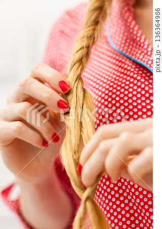 Closeup of woman doing braid on blonde hair 136364986