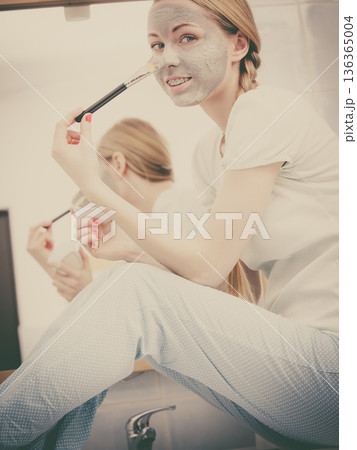 Woman applying with brush clay mud mask to her face 136365004