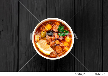 Solyanka soup with sausage, olives and lemon in kraft bowl with sour cream on dark table 136366123