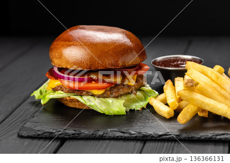 Beef cheeseburger with lettuce, tomato and onion, served with fries and ketchup on slate board Beef cheeseburger with lettuce, tomato and onion, served with fries and ketchup on slate board 136366131