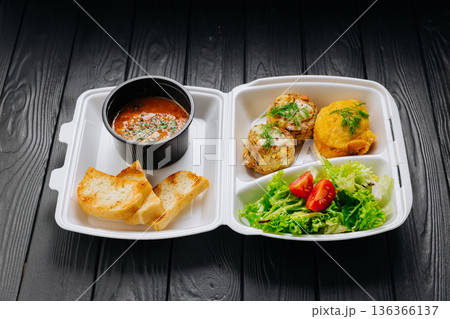 Takeaway lunch box with tomato soup, salad and cutlets on dark wooden table Takeaway lunch box with tomato soup, salad and cutlets on dark wooden table 136366137