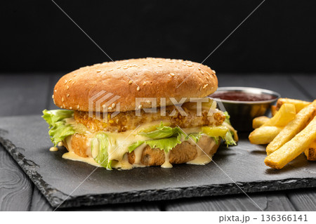Crispy chicken burger with lettuce and melted cheese sauce, fries and ketchup , dark background Crispy chicken burger with lettuce and melted cheese sauce, fries and ketchup , dark background 136366141