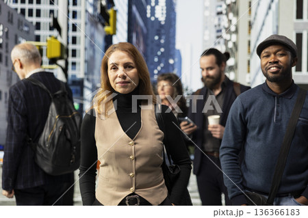 Portrait of businesswoman with formal clothes standing on the sidewalk in crowded city center, walking across metropolitan area business district. Female professional on a busy street. Portrait of businesswoman with formal clothes standing on the sidewalk in crowded city center, walking across metropolitan area business district. Female professional on a busy street. 136366183