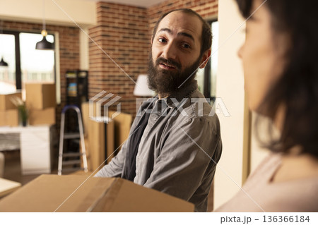 Bearded white man with girlfriend arriving at recently purchased home, holding cardboard boxes and stepping into new living space. Caucasian couple moving in with packed belongings. Bearded white man with girlfriend arriving at recently purchased home, holding cardboard boxes and stepping into new living space. Caucasian couple moving in with packed belongings. 136366184