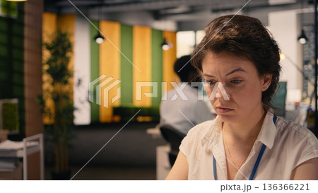 Frowning businesswoman with confused and skeptical expression at desk, appearing uncertain and indecisive reviewing visual data on laptop. Undetermined irregular performance metrics, confusion. 136366221