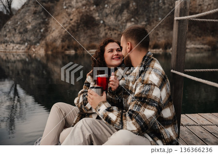 Couple shares warm drinks on a dock by a lake during a quiet moment together on Valentines Day Couple shares warm drinks on a dock by a lake during a quiet moment together on Valentines Day 136366236