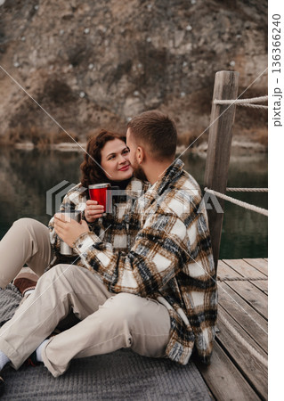 Couple enjoys warm drinks by the lakeside on Valentines Day while dressed in cozy outfits Couple enjoys warm drinks by the lakeside on Valentines Day while dressed in cozy outfits 136366240