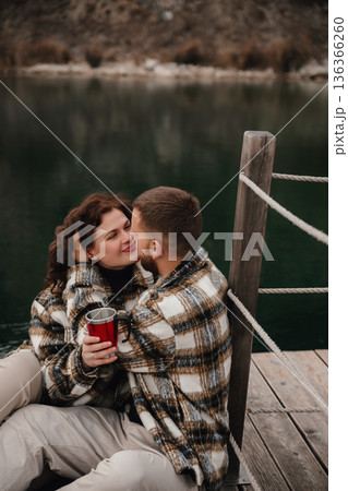 Couple enjoys quiet moment on dock with hot drink while celebrating love during winter season 136366260