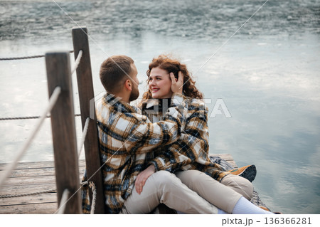 Couple sitting on wooden dock by water sharing moments on a cloudy day 136366281