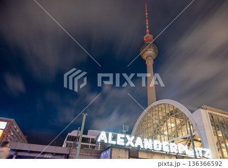 Berlin, germany, august 12, 2023. Berlin cityscape at night with illuminated fernsehturm and alexanderplatz station under streaking clouds, long-exposure urban glow 136366592