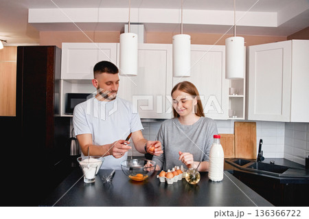 Couple prepares breakfast in a modern kitchen while cracking eggs and mixing ingredients for a meal 136366722