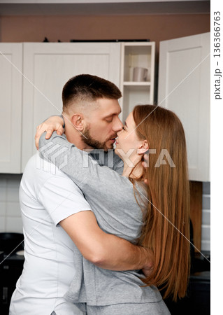 Couple shares a moment in the kitchen during the evening while preparing dinner together in a cozy home setting Couple shares a moment in the kitchen during the evening while preparing dinner together in a cozy home setting 136366763