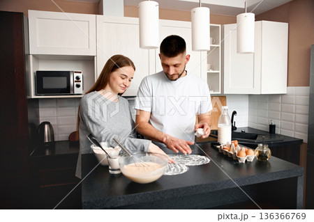 Couple preparing food together in a modern kitchen during the morning hours while smiling and enjoying each others company 136366769