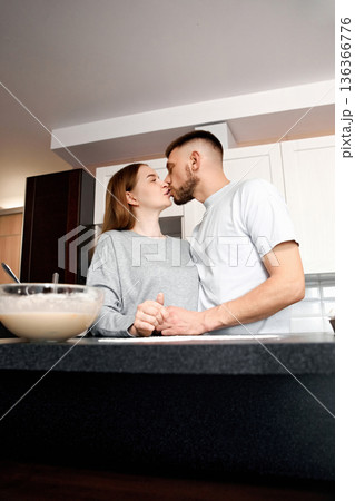 Couple shares a kiss in the kitchen while preparing food together in a modern home setting during the day 136366776