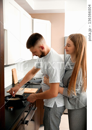 Couple cooking together in a modern kitchen during the evening while enjoying each others company Couple cooking together in a modern kitchen during the evening while enjoying each others company 136366804