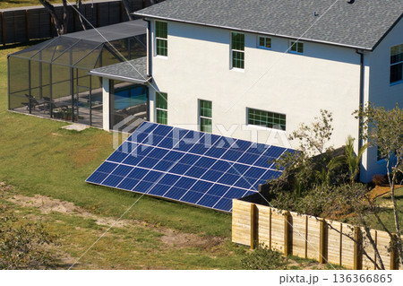 Residential house with solar photovoltaic panels for producing of clean ecological electrical energy mounted on backyard ground in suburban rural area. Concept of autonomous home 136366865