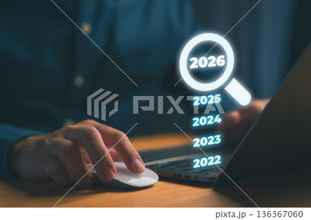 Person using laptop with glowing magnifying glass highlighting 2026 among past years, symbolizing vision, future planning, focus, innovation trends, digital strategy, and goal forecasting. 136367060