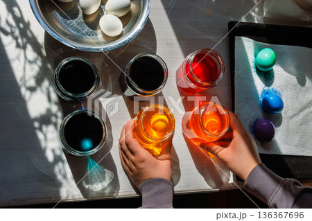 Top view of the hands arranging dye jars for easter egg coloring on sunlit table. 136367696