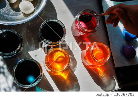 Spoon lifting pink dyed egg from jar in sunlit easter egg dyeing setup 136367703