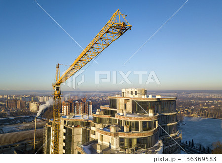 Apartment or office tall building under construction, top view. Tower crane on bright blue sky copy space background, city landscape stretching to horizon. Drone aerial photography. Apartment or office tall building under construction, top view. Tower crane on bright blue sky copy space background, city landscape stretching to horizon. Drone aerial photography. 136369583