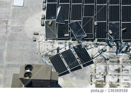 Top view of destroyed by hurricane Ian photovoltaic solar panels mounted on industrial building roof for producing green ecological electricity. Consequences of natural disaster in Florida 136369588