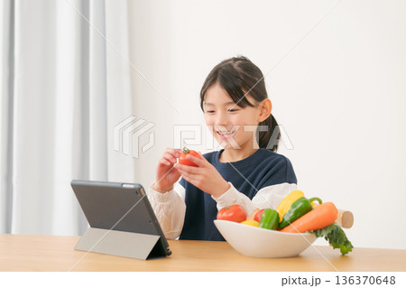 タブレットを見ながら野菜を持つ女の子 136370648