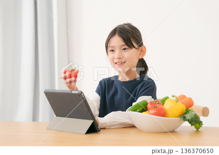 タブレットを見ながら野菜を持つ女の子 136370650