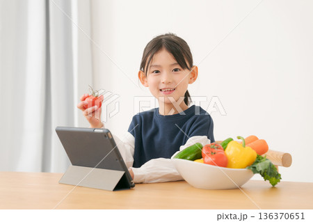 タブレットを見ながら野菜を持つ女の子 136370651