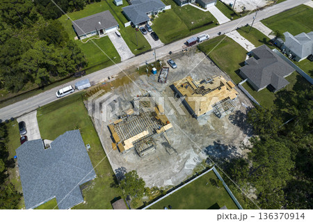 Aerial view of builders working on unfinished residential house with wooden roof frame structure under construction in Florida suburban area Aerial view of builders working on unfinished residential house with wooden roof frame structure under construction in Florida suburban area 136370914