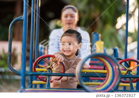 child girl with mother playing with a steering wheel toy on a playground child girl with mother playing with a steering wheel toy on a playground 136372817