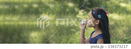 Adorable happy cute girl playful foam bubbles in green playground in summer outdoors. Funny Cheerful girl in the park happiness times. Bubbles blowing soap playful in nature park. Adorable happy cute girl playful foam bubbles in green playground in summer outdoors. Funny Cheerful girl in the park happiness times. Bubbles blowing soap playful in nature park. 136373217