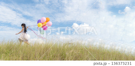 Banner Cheerful cute girl holding balloons running green meadow white cloud and blue sky with happiness. Panorama Hands holding vibrant air balloons happy times summer sunlight outdoor copy space 136373231