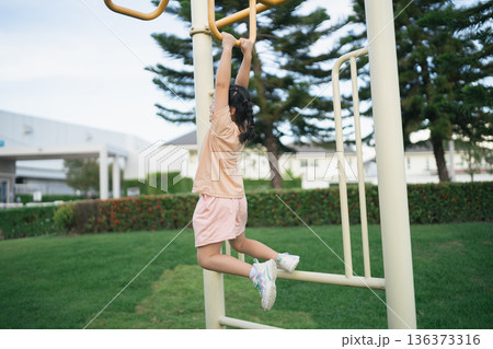 Young girl hanging on monkey bars in a sunny park, playground equipment, active childhood, outdoor fun, cheerful exercise, nature background, children's playtime Young girl hanging on monkey bars in a sunny park, playground equipment, active childhood, outdoor fun, cheerful exercise, nature background, children's playtime 136373316