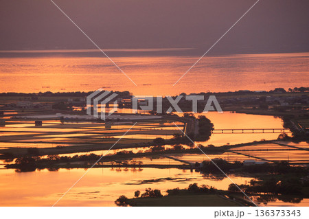 滋賀県東近江市猪子町の猪子山から望む水張りの田植え前の水田がオレンジ色に光る夕景 136373343